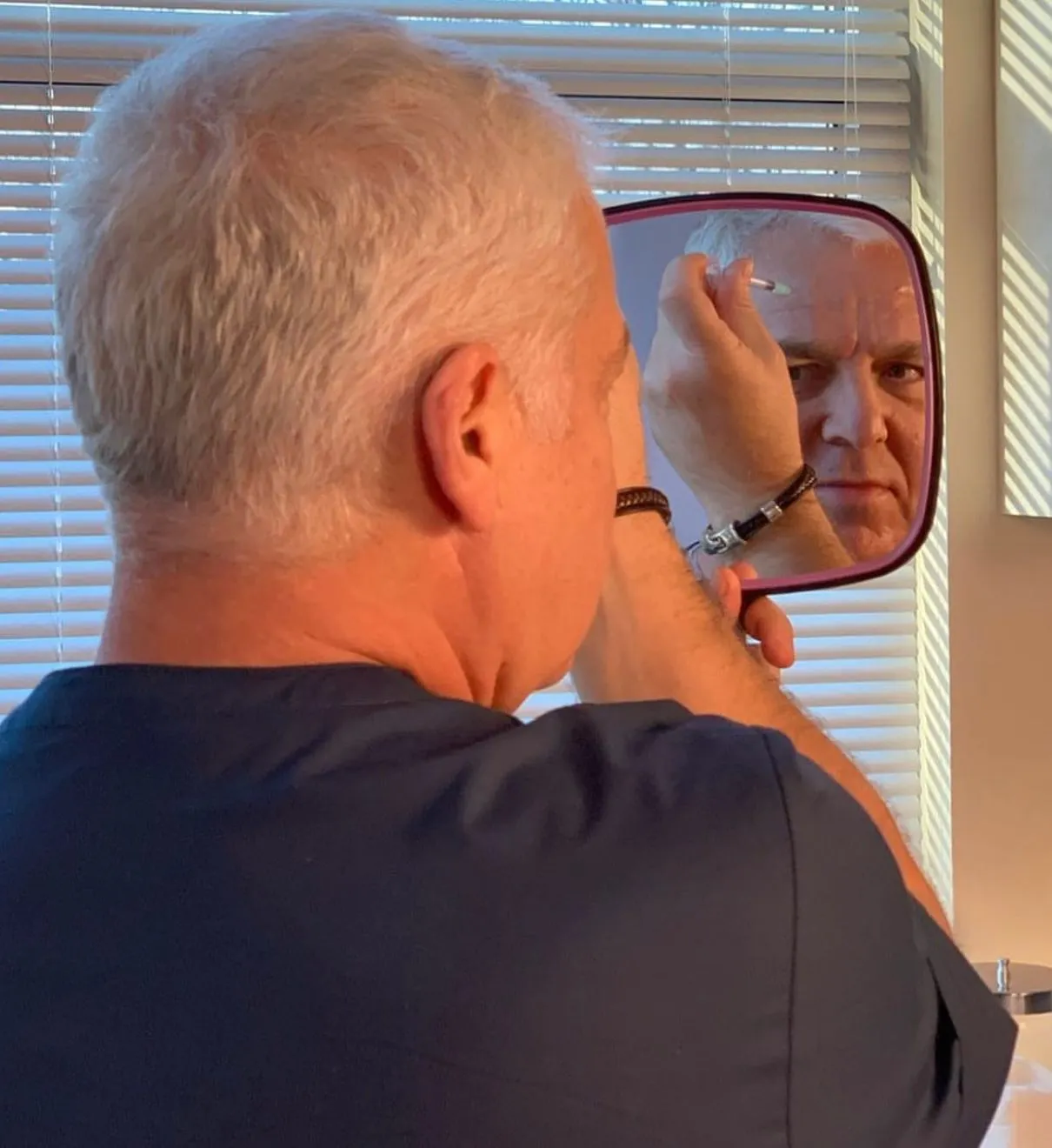 Male patient examining his facial profile in a handheld mirror during a Botox consultation